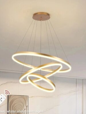 إضاءة مودرن بتصميم نورديك فخم من 3 حلقات ذهبية، مع تحكم كامل بالريموت لتغيير الإضاءة بين الدافئ، الطبيعي، والبارد. مناسبة لغرف السفرة، الصالونات، والنمط الفندقي الفاخر.