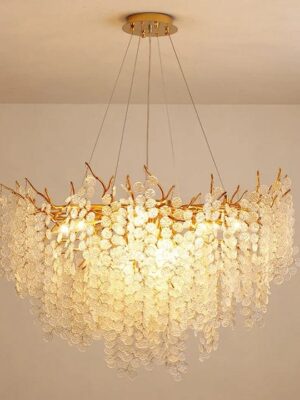 نجفة أوراق كريستال دائرية بتصميم فاخر يجمع بين الجمال واللمسات الفنية. هيكل معدني مطلي باللون الذهبي مع أوراق كريستالية متدلية تمنح إضاءة دافئة ومظهرًا مميزًا يخطف الأنظار. مثالية لغرف المعيشة، السفرة، أو أي مساحة تحتاج لإضاءة راقية تضيف فخامة وأناقة حقيقية للمكان.